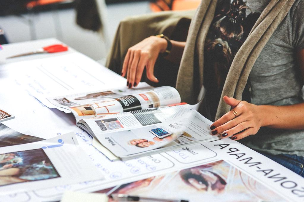 Stack of fashion and lifestyle magazines next to a laptop with coffee cup
